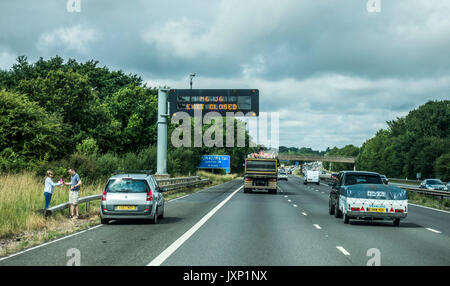 Une voiture en panne et un couple à proximité, sur la bande d'arrêt d'urgence de l'autoroute M6 dans les East Midlands, cap à l'ouest, Angleterre, Royaume-Uni. Banque D'Images