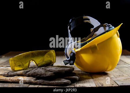 Casque jaune et gants de soudeur. Fond noir et de la vieille table en bois. Banque D'Images