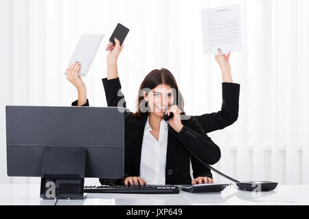 Femme d'occupé le multitâche At Desk In Office Banque D'Images