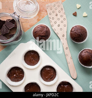 Muffins au chocolat sur une table en bois avec cuisine, un pot plein de pièces en chocolat et des chocolats en forme de coeur. Vue d'en haut. Format carré. Banque D'Images