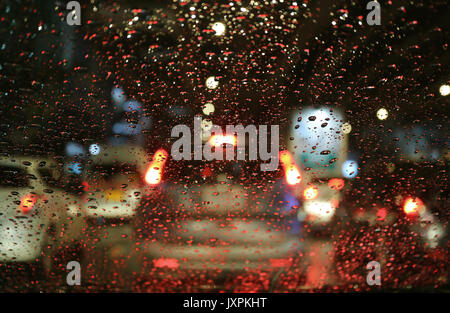Lumières de rue floue et les feux arrière à travers les gouttes de pluie sur le pare-brise de voiture dans la nuit Banque D'Images