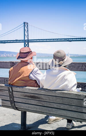 San Francisco senior couple au Ferry Building s'asseoir et regarder une vue sur le Bay Bridge. Vu de l'arrière. Banque D'Images