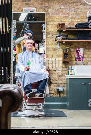 Hipster homme boire une bière après avoir couper les cheveux à Shoreditch, London, England Banque D'Images