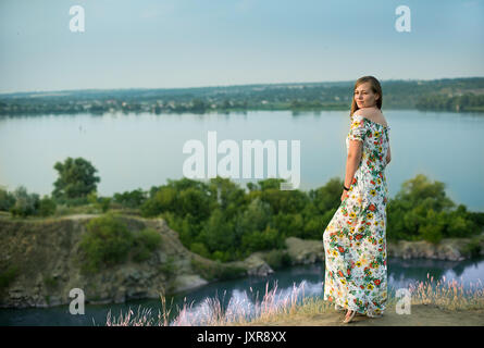 Toute la longueur du positif charmante femme vêtue de blanc longue robe d'été happy smiling en fond coucher de soleil. Belle femme profiter. Banque D'Images