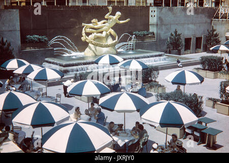 Les gens boire et manger dans la partie inférieure de la Plaza Rockefeller Center, New York, en 1956. Image montre la mode des années 50, période. Statue de Prométhée dans l'arrière-plan. Banque D'Images