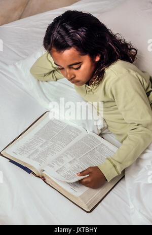 Enfance enfant ethnique reading Bible au lit Jeune Fille 7-10 ans Africain/Caucasian United States Myrleen Pearson Banque D'Images