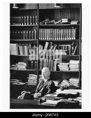 John Hallock Berthel, photographie de portrait, assis, taille haute, vue de trois quarts, derrière le bureau et devant la bibliothèque, 1960. Banque D'Images