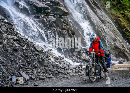 Femme passant l'une des nombreuses cascades tout en vélo à travers la gorge du tigre bondissant, province du Yunnan, Chine Banque D'Images