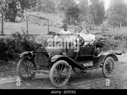 Portrait complet de deux hommes conduisant une voiture à l'extérieur, un enfant afro-américain dans la voiture, 1920. Banque D'Images