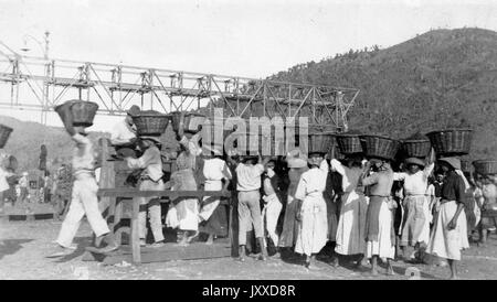 Un grand groupe de travailleurs afro-américains se tient à l'extérieur portant des paniers en osier sur leur tête, 1915. Banque D'Images