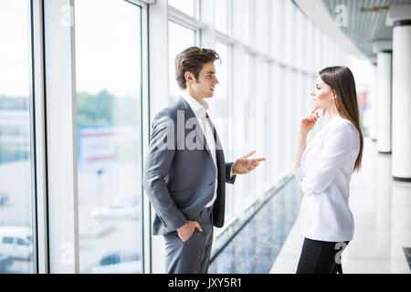 Deux youngbusinessman womanare et d'affaires debout dans un bureau moderne, doté de fenêtres panoramiques. Banque D'Images