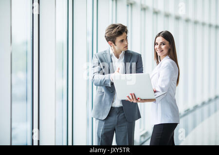 Businessman and businesswoman using a laptop together while standing in front of office building windows Banque D'Images