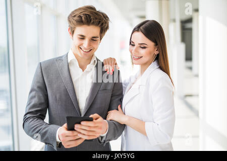 Deux hommes d'affaires élégant smiling man en costume formel et la femme en robe et veste à la recherche sur l'office de fenêtre près de l'intérieur Banque D'Images