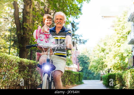 Senior man riding bicycle avec sa petite-fille dans ses mains Banque D'Images