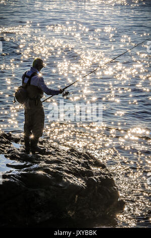 Les chefs d'un homme à la pêche tôt le matin alors que la marée est haute,et le soleil se reflète sur les petites vagues qui les rend ressemblent à de petites étoiles. Banque D'Images