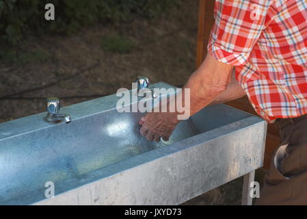 Vieil homme en chemise à carreaux de laver ses mains outdoor Banque D'Images