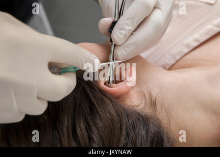 Faire un trou de piercing professionnel sur l'oreille avec canule à demeure la méthode. Type de tour. L'oreille de préhension Banque D'Images