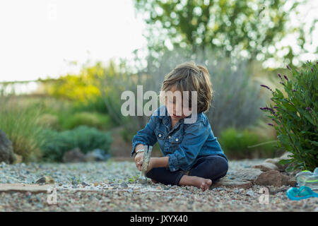 Young boy sitting on ground smashing roches avec hammer Banque D'Images