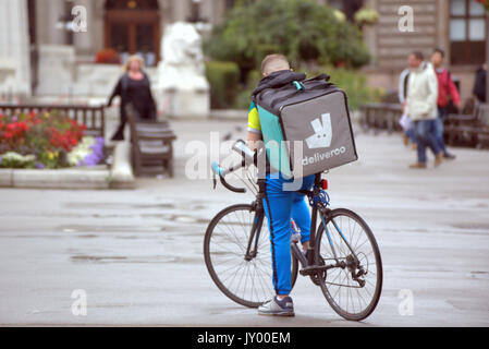 Wet george square Glasgow garçon jeune homme deliveroo cycliste vélo livraison livraison alimentaire sms en attente de travail en ce qui concerne la prestation de l'extérieur, sur la route de rue Banque D'Images