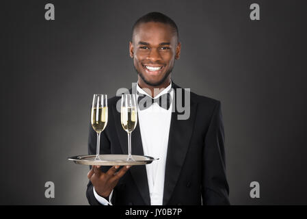 African Waiter Holding Champagne verre sur fond noir Banque D'Images