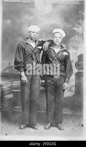 Portrait debout de deux jeunes Afro-américains aux expressions neutres devant un fond peint avec une scène portuaire, vêtu de la tenue du marin, 1920. Banque D'Images