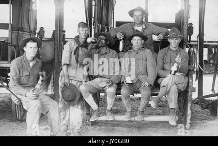 Un groupe de travailleurs américains aux expressions neutres est rassemblé devant et sur un wagon, buvant de l'alcool à partir de bouteilles de verre, 1915. Banque D'Images