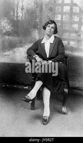 Séance pleine longueur portrait, young African American Woman, portant robe sombre avec la lumière un chemisier, assis en face de toile, expression neutre, 1920. Banque D'Images