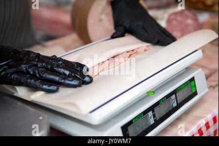 Le vendeur sur le marché avec des gants roulés saucisses sur la balance Banque D'Images