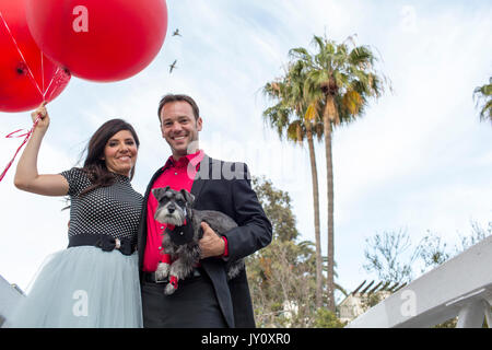 Smiling couple holding dog et red balloons Banque D'Images