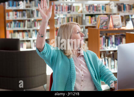 Caucasian woman using computer in library raising hand Banque D'Images