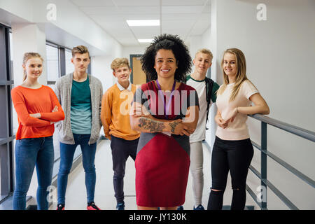 Enseignante de tatouages pose pour la caméra avec ses bras croisés. Il y a des étudiants dans l'arrière-plan qui sont également posant pour la caméra. Banque D'Images