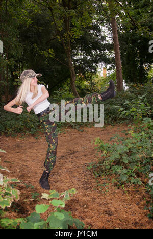 Adolescente blonde dans un endroit de la forêt portant des pantalons de camouflage et un t-shirt blanc Banque D'Images