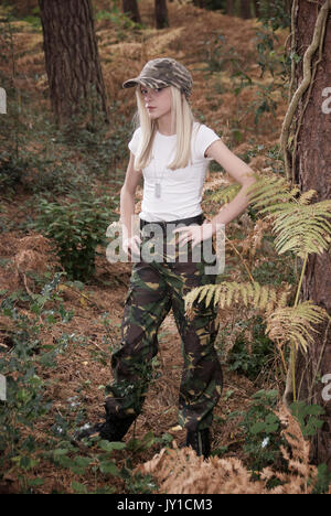 Adolescente blonde dans un endroit de la forêt portant des pantalons de camouflage et un t-shirt blanc Banque D'Images