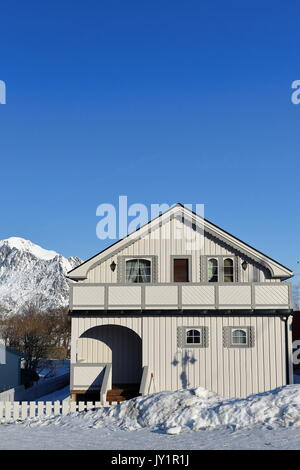 Chalet en bois blanc avec couloir et d'une terrasse et entourée de clôture Blanche-neige Reine village en hiver. Festhaeltinden montagne en arrière-plan. Banque D'Images