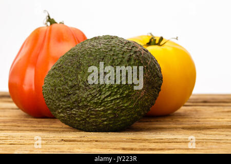 Deux heirloom tomatoes et un avocat dans un regroupement sur une planche à découper, fond blanc. Une tomate est rouge et l'autre est jaune. Banque D'Images