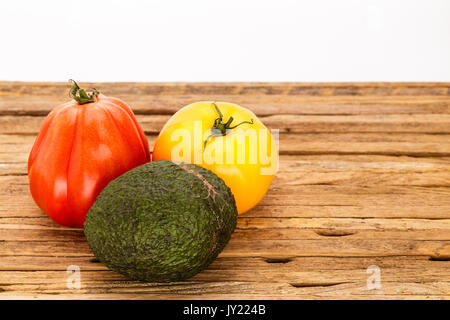 Deux heirloom tomatoes et un avocat dans un regroupement sur une planche à découper, fond blanc. Une tomate est rouge et l'autre est jaune. Banque D'Images