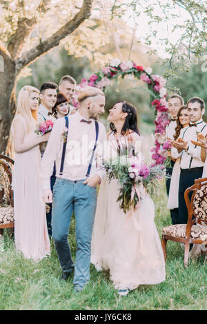 La photo en gros plan de la très belle cérémonie de mariage bois ensoleillé. Le smiling young couple à l'arrière-plan des invités et l'arche de mariage Banque D'Images