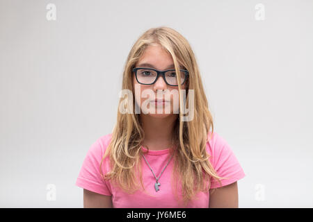 Portrait d'un très sévère et sérieuse peu jolie fille sur un t-shirt rose et des lunettes sur un fond blanc Banque D'Images