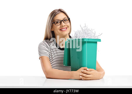 Jeune femme avec une poubelle pleine de papier déchiqueté assis à une table isolé sur fond blanc Banque D'Images