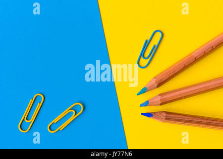 Trois crayons en bois avec une pointe de bleu et bleu et jaune des trombones contre un fond bleu et jaune avec copie espace pour le texte. Banque D'Images