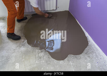 Vacances en construction. travailleur met une chape d'auto-nivellement sur plancher de béton Banque D'Images