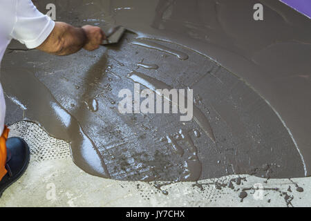 Vacances en construction. travailleur met une chape d'auto-nivellement sur plancher de béton Banque D'Images