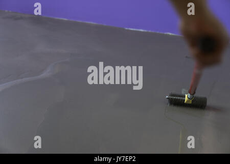 Vacances en construction. travailleur met une chape d'auto-nivellement sur plancher de béton Banque D'Images