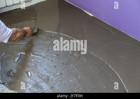 Vacances en construction. travailleur met une chape d'auto-nivellement sur plancher de béton Banque D'Images