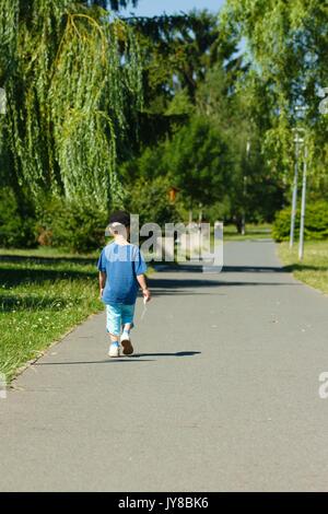 Les petit enfant dans la rue et de l'habillement sportif black hat s'éloigner de la caméra dans un parc Banque D'Images