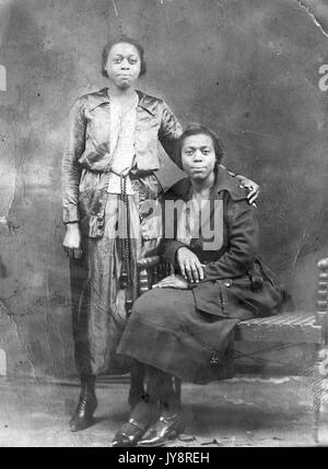 Portrait de deux femmes afro-américaines avec des expressions neutres, un article portant un chemisier, veste, jupe et l'autre, assis sur un banc, vêtu d'un manteau foncé longueur de plancher, 1915. Banque D'Images