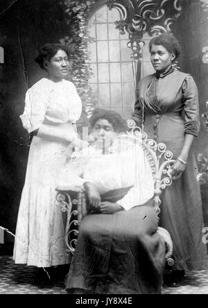 Portrait de trois femmes afro-américaines, deux debout derrière l'autre assis dans une chaise, arborent des posés en face d'une fresque-comme toile de fond, la femme la plus à gauche dans une robe blanche, et les deux autres en robes sombres, avec toutes les expressions du visage en blanc, 1920. Banque D'Images