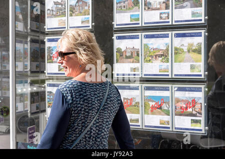 Femme à la recherche dans une fenêtre de l'agent immobilier à immobilier à vendre. England UK Banque D'Images