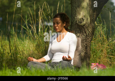 Femme faisant une méditation dans la nature tout en s'appuyant contre un arbre Banque D'Images