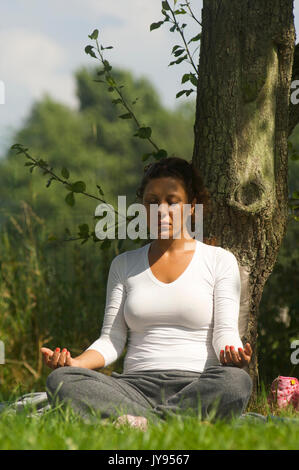 Femme faisant une méditation dans la nature tout en s'appuyant contre un arbre Banque D'Images